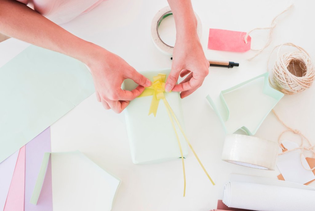 overhead-view-woman-sticking-yellow-ribbon-wrapped-gift-box.jpg